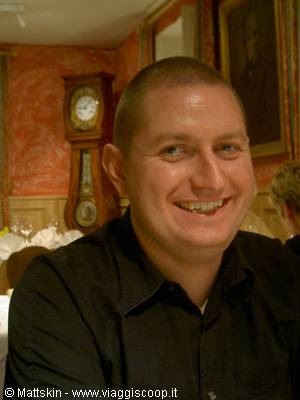 Smiling man in black shirt, behind him a grandfather clock and red walls
