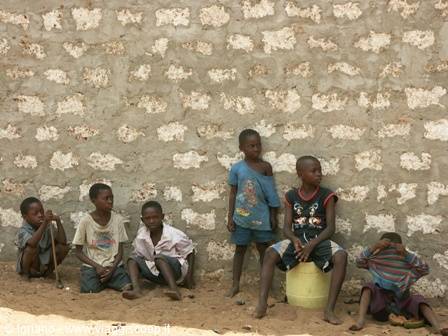 Children sitting against a rough stone wall, one standing