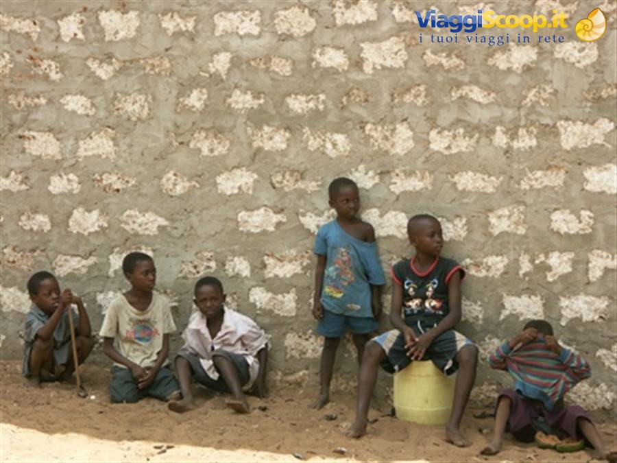 Children sitting against a rough stone wall, one standing