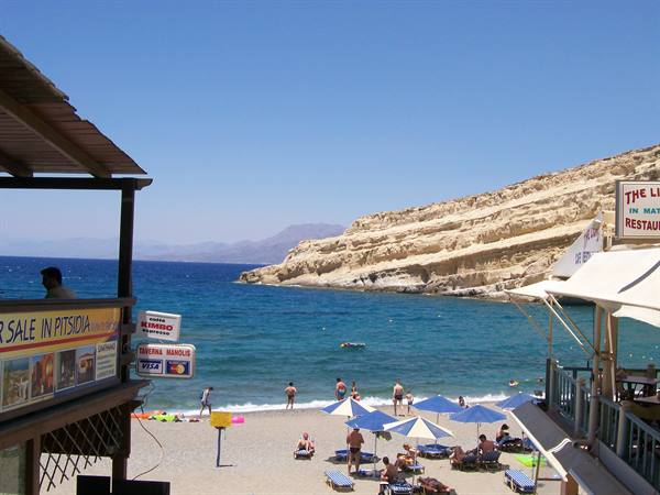 Pitsidia beach, blue umbrellas and swimmers beneath golden cliffs