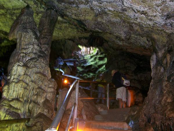 Tourists on a metal staircase inside a limestone cave lit by artificial lights