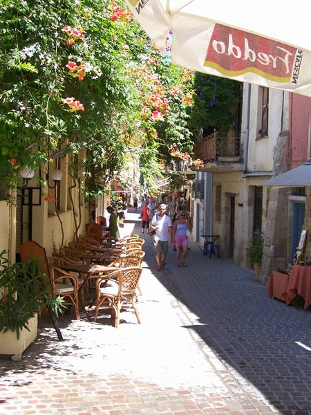 Stone alley with wicker café chairs, climbing flowers and strollers under the awning