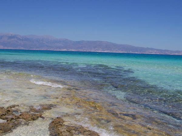 Crystal turquoise water over rocks, arid mountains on the horizon, Elafonisi