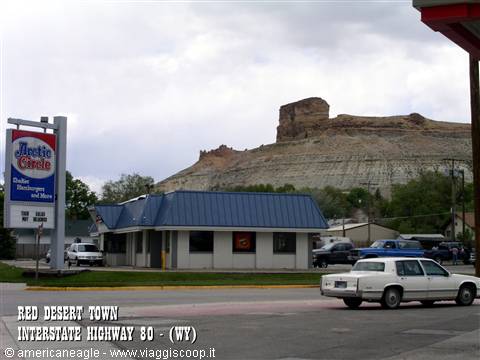 Restaurant circa 1900 below eroded rock formation, parked cars, gray sky