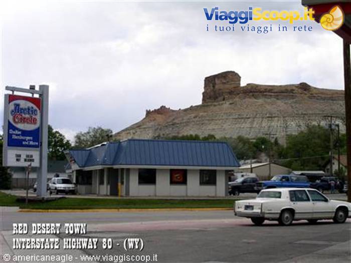 Restaurant circa 1900 below eroded rock formation, parked cars, gray sky