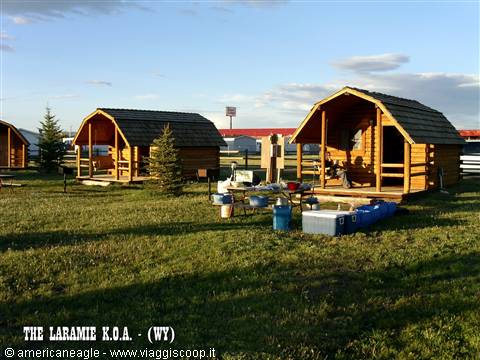 Wooden camping cabins at Laramie KOA, green lawn, coolers and gear in front