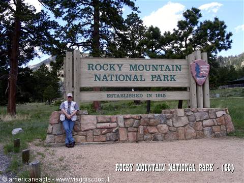 Tourist leaning on the stone wall beneath the wooden Rocky Mountain National Park sign