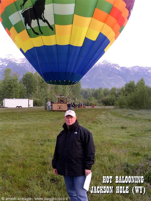 Man in front of colorful moose hot air balloon, grassy field and snowy mountains, Jackson Hole
