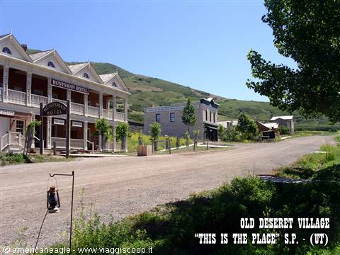 Dirt street with white wooden Hunters Hotel, western village beneath green hills