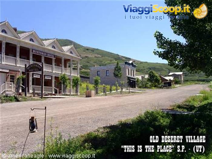 Dirt street with white wooden Hunters Hotel, western village beneath green hills