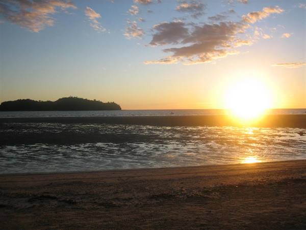 Dark island over the sea, low sun lights clouds and wet sand