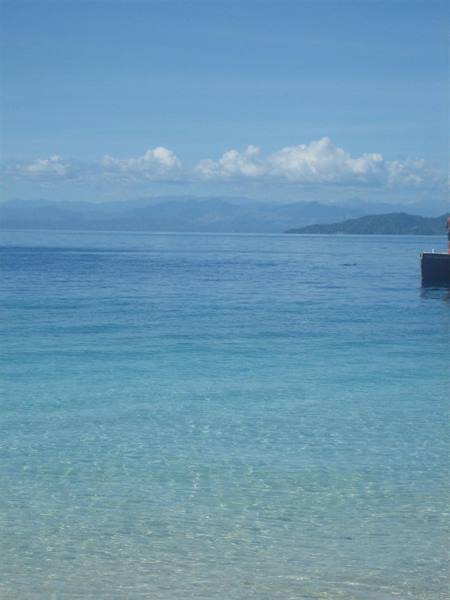 Clear turquoise water over sandy shore, boat at right, mountains on horizon