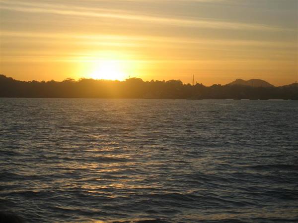 Low sun behind tree-lined shore, dark rippled water in the foreground
