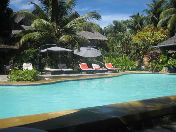 Turquoise pool with loungers and umbrellas among palms and bungalows