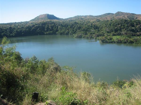 Green lake surrounded by forested hills, dry grass in foreground, clear sky