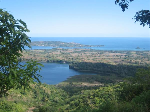 Green foliage frames a blue lake and sunlit coastline with distant islands