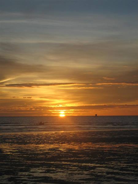 Lone boat on shimmering sea at horizon, golden sky above the beach