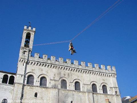 Gubbio: figure glide on cable in front of Palazzo dei Consoli, clear blue sky