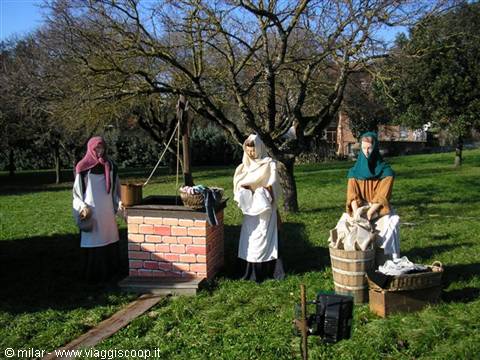 Costumed mannequins beside a brick well on a grassy park lawn
