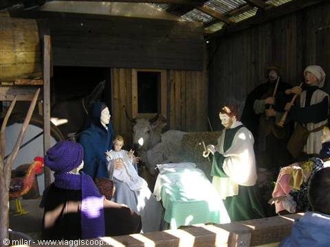 Life-sized nativity scene statues inside a wooden stable, sunlight streaming in
