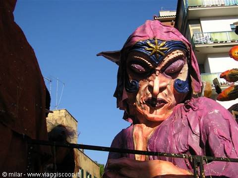 Carnival float with giant purple witch mask among the buildings