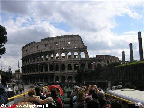 Tourists on an open bus photograph the Colosseum under cloudy skies