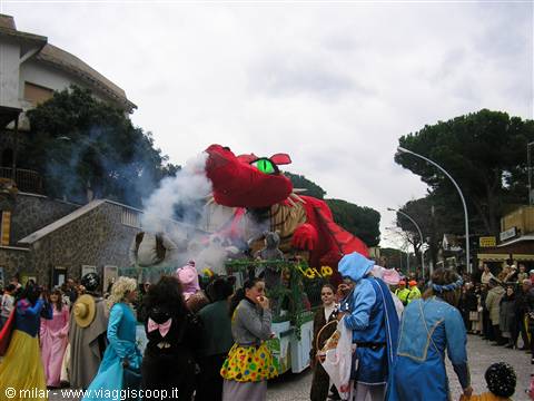 Red dragon-shaped carnival float spewing smoke, crowd in costumes on the street