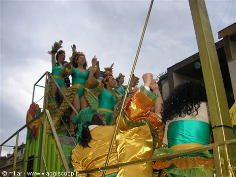 Dancers in green and gold costumes waving from a carnival float