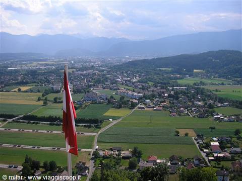 Red flag on pole above village with green fields and alpine mountains