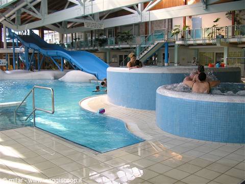 Indoor pool with blue slide and tiled hot tubs, people relaxing