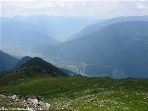 Alpine valley with grassy slope and stones in foreground, hazy mountains beyond