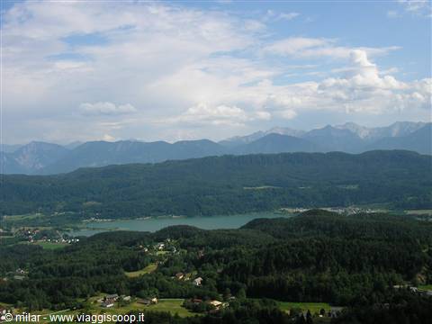 Faak lake surrounded by forests and mountains under white clouds