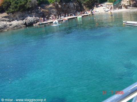 Turquoise bay with rocky shore and swimmers on a wooden pier