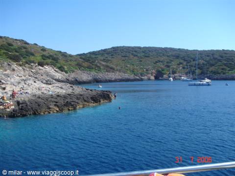 Rocky cove with turquoise water, anchored sailboats and swimmers on the rocks