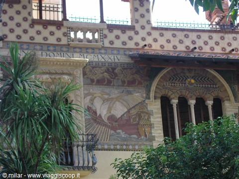 Facade with medieval ship mosaics, stone loggia, palm leaves in foreground