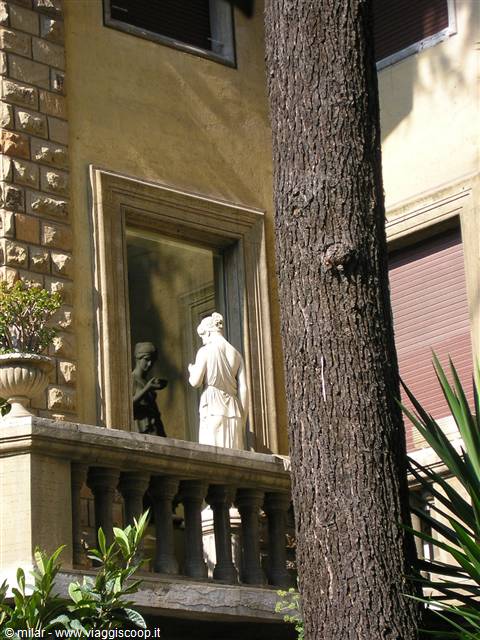 White marble statue of a woman on a stone balcony beside a tall pine