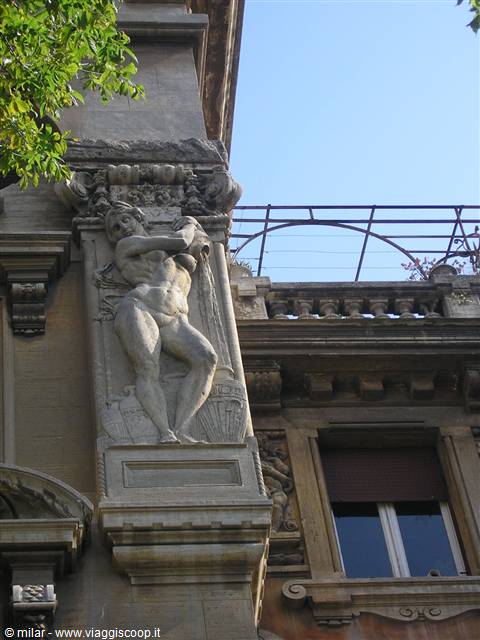 Stone statue of nude woman on a building facade, blue sky and green leaves