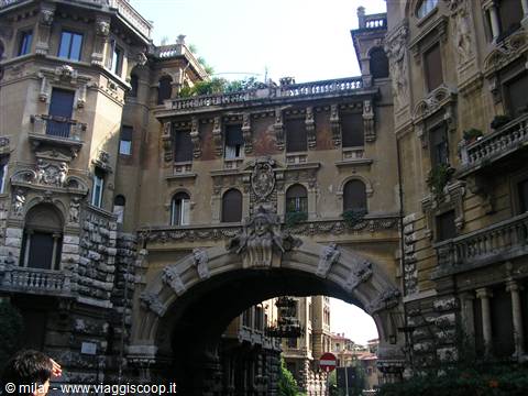 Stone arch between ornate Art Nouveau buildings with statues and balconies