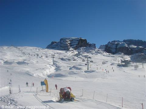 Snow groomer and ski lift on a Dolomites slope under rocky peaks