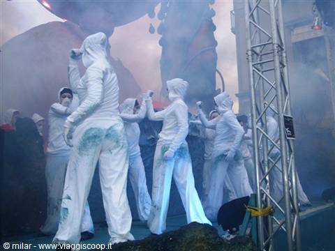 Performers in white suits amid blue smoke on carnival stage