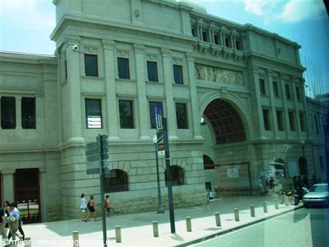 Light stone facade of Milano Centrale station, pedestrians and cars under the arch