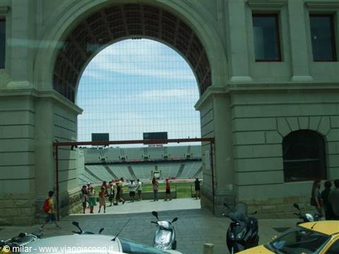 Visitors under Barcelona Olympic Stadium arch, stands and scooters in foreground