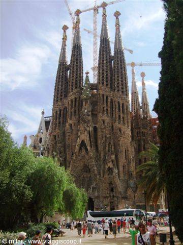 Tourists admire the Sagrada Família among trees and construction cranes