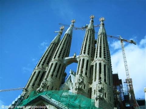 Sagrada Familia spires with cranes and scaffolding against a blue sky