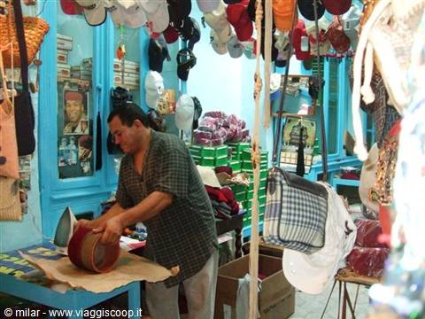 Vendor cleaning red hat in his blue shop, caps hanging everywhere