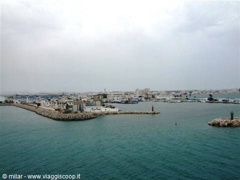 Harbor with stone breakwaters, white docks and sun under clouds