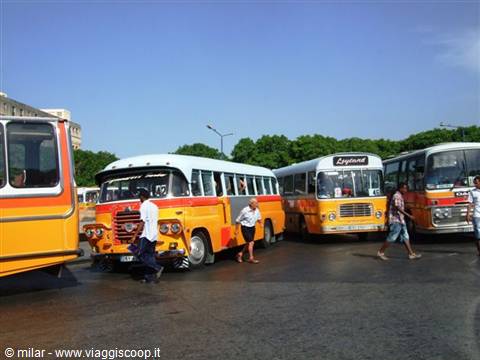 Orange buses parked at a bus station, passengers boarding in sunlight