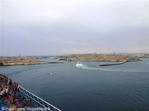 Passengers on the ship deck watch a ferry enter Valletta's Grand Harbour