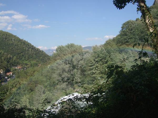 A rainbow crosses the green trees above a waterfall among the hills