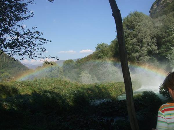 A boy watches a rainbow over Marmore Falls among the trees